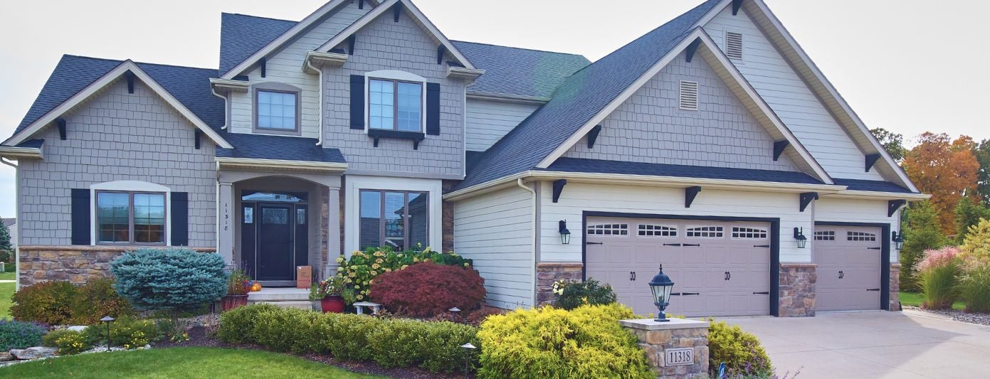 Large new build home surrounded by green grass, and planted shrubs. 